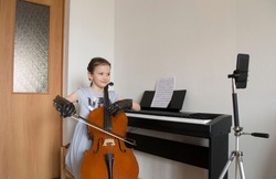 Musician girl in gray dress and gloves playing classic cello at home, online musical class, distance education at Covid-19 Coronavirus quarantine, self-isolation, online learning, home school concept