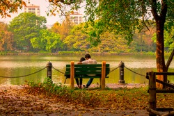 Young Couple sitting in an autumn park bench in Lakeshore. Falling in love in Maple leaf garden. Relaxation and romantic activity surrounded by Beauty in nature.