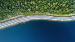 Beautiful aerial view of road between green summer forest and blue lake in Lapland.