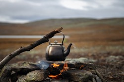 Small kettle is heated on a bonfire. Hiking, travel in the mountains. Outdoor recreation concept. Lapland.