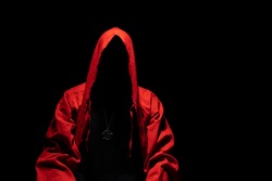 Mystic red hooded person in the darkness. Pentagram pendant on the chest. Satanic ,occult, esoteric and black magic concept. Copy space.
