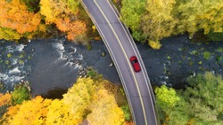 Aerial view of road and bridge over river with red car in yellow and orange autumn forest in rural Finland.