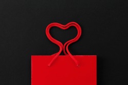 Red shopping bag with heart shape rope on dark background. Purchase, Love, Valentine, Sale, Black friday concept. Top view, copy space, mock-up