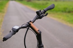 Concept riding a bike alone in nature: close-up of a bicycle handlebar of an e-bike in the foreground, bike path and green nature in the blurred background