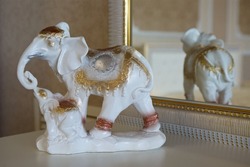 A porcelain figurine of a white elephant with a baby elephant stands on the surface of the table near the mirror.