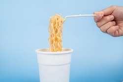 A cup of hot instant noodle on light blue background. Hot instant noodles is a cheap ready to eat food. 
