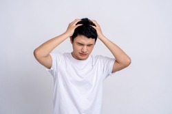Young Asian man wearing white t-shirt touching head temples experiencing stress having troubles difficulties to resolve issues, He has a headache and panic on a studio white background.