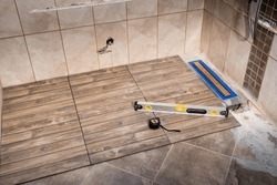 Linear floor level shower. Wood effect ceramic tile and modern metallic linear drain installation in the bathroom