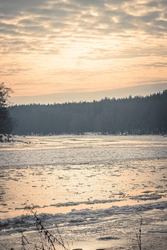 Colorful sky over Neris river, Lithuania. Vertical waterscape view on a sunny January day. Ice flowing on the surface of water. Selective focus on the details, blurred background.