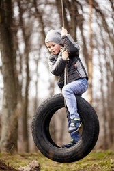 Happy child swinging on a car tire used as a swing. Concept photo of childhood.