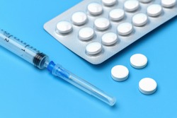 Pills and a syringe. Tablets in a plastic blister on blue background. Vaccination against coronavirus