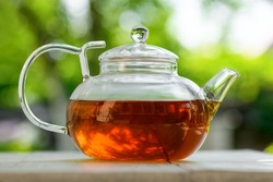 Tea in a glass teapot on a green background. Teapot with green or black tea with reflection in glass in the country. Tea time