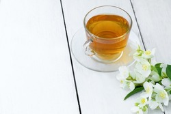 Jasmine tea in glass cup and flowers on a wooden white background. Cup with green jasmin tea. Tea time