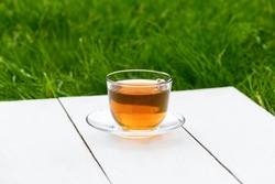 Tea in a glass cup on a white wooden background against the backdrop of green grass. Teapot with green or black tea. Tea time