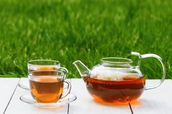 Jasmine tea and flowers in glass teapot and two cups on a wooden white background against the background of green grass. Herbal tea