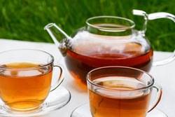 Tea in glass teapot and two cups on a wooden white background background against the background of green grass. Teapot with green or black tea. Tea time