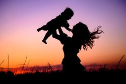 Silhouette happy mother and baby. Mother plays with her baby in her arms under the rays of the sunset in a meadow. Motherhood concept. Happiness, inspiring, joyful moments. Mother's day concept.