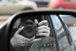 Reflection in side view mirror of someone with DSLR camera. Hidden photographing, paparazzi concept
