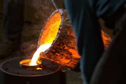Molten bronze poured into mold by melter in foundry workshop