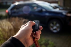 A close up portrait of a person holding a car key in his hand pressing the unlock button. The keyless remote control has unlock and lock icons for the doors and the trunk of the vehicle.