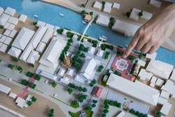 finger pointed to mass model of landscape design or garden design or landscape architecture in waterfront temple area with group of buildings and trees in community,  bird's eye view, selective focus