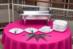 Table decorated with pink tablecloth, plates, cutlery and Rechaud at a birthday party