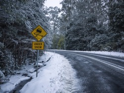 Slippery road warning sign for car drivers on side of a snow covered road. Icy scenic mountain route in winter forest. Mt Donna Buang, VIC Australia