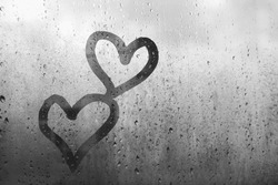 Two hearts drawn on window glass by finger, black and white, fogged with raindrops