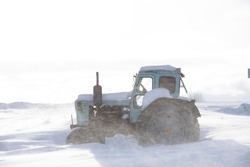 Tractor on a deserted snow-covered field against a cloudy sky. Poor visibility due to a snowstorm.