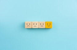Customer service evaluation and satisfaction survey concepts, evaluation, Increase rating. Happy face smile face icon on wooden cube on blue background