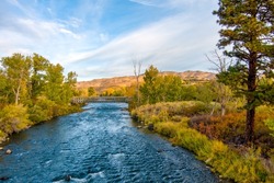 Aerial view of a beautiful River in Autumn with colorful trees, barren desert mountains, and a partly cloudy blue sky near Reno Nevada.