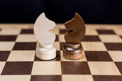 Two chess knights are facing each other on the chessboard. The concept of rivalry, duel, battle, struggle, two opposing sides, enemies, opposition, enmity.