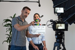 Behind the Scenes on a Video Production Set. Director Uses Clapper Slate to Signify Action. Video Camera, Microphone and Lighting Can Be Seen During Interview