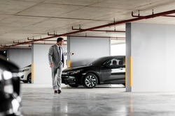 Portrait of middle-aged businessman leaving his black car in a parking garage. Horizontal shot