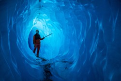 Man inside a melting glacier ice cave. Cut by water from the warming, melting glacier, the cave runs deep into the ice of the Matanuska Glacier in Alaska.