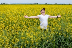 A farmer standing in rapeseed (oilseed) field with his arms spread, looking at the sky hoping for the rain, and a good yield. Relationship between agronomy and weather forecast for yield estimation.