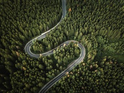 Aerial view of countryside road passing through the green forest and mountain