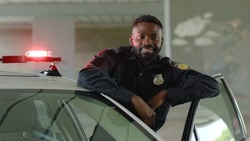 Smiling african american young man cops stand near patrol car look at camera enforcement happy officer police uniform auto safety security communication control policeman close up slow motion