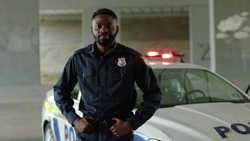 Close up smiling african american young man cops stand near patrol car look at camera enforcement happy officer police uniform auto safety security communication control policeman portrait slow motion