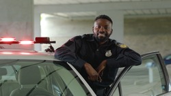 Close up smiling african american young man cops stand near patrol car look at camera enforcement happy officer police uniform auto safety security communication control policeman portrait slow motion