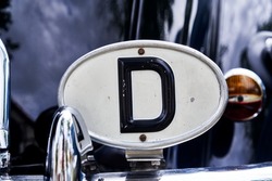 Oval badge made of white sheet metal with black letter D to mark the country of origin Germany on a car