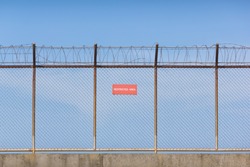 Wire mesh fence and a restricted area sign with blue sky background
