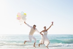 Newlyweds having fun holding balloons at the beach