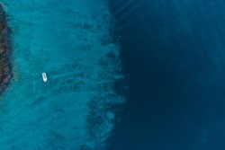 Aerial view of a boat floating by the coast above deep blue see