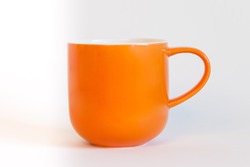 side view of empty orange cup with handle on white