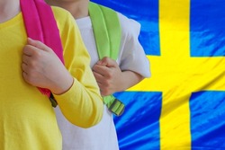 Two children with satchels background of Sweden flag. Concept of upbringing and educating children in Sweden