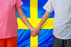 Two children joined hands on flag Sweden background. Boy and girl joined hands on background flag of Sweden. Concept of family and parenting in Sweden