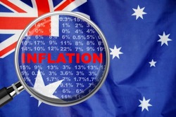 Magnifying glass focused on the word inflation on Australia flag background. Hike interest rate. Inflation income crisis. Inflation, tax, cash flow and another financial concept in Australia