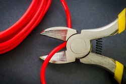 Pliers tool cutting red electric wire closeup on black background, service and repairing concept
