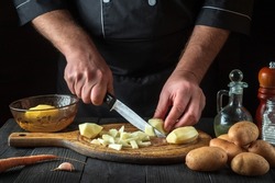 Before preparing the national dish, the chef cuts raw potatoes into small pieces with a knife. Close-up of a cook hands while working in a restaurant kitchen.